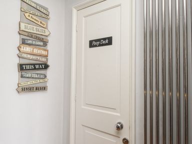 A white door with a poop deck sign a vertical metal radiator and a wall with wooden direction signs at Harbourside House in Brewers Quay Harbour