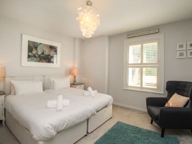 A bedroom with two single beds bedside tables with lamps a window and an armchair at Harbourside House in Brewers Quay Harbour