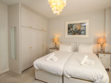 A bedroom with two single beds white linens bedside tables lamps and built in wardrobes at Harbourside House in Brewers Quay Harbour