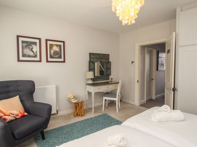 A bedroom with a dark armchair a small desk and chair twin beds with rolled towels at Harbourside House Brewers Quay Harbour