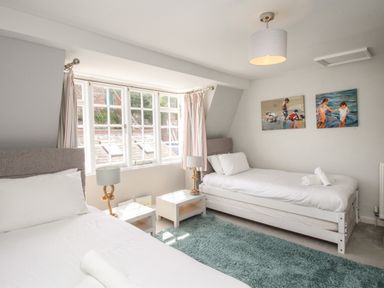 A bedroom with two single beds a window rug and paintings at Harbourside House in Brewers Quay Harbour