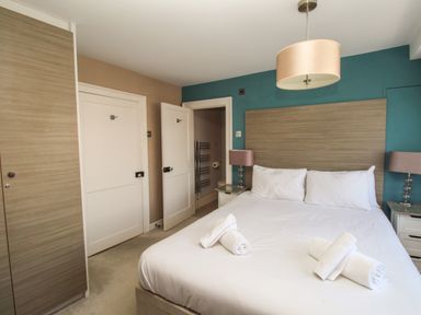 A bedroom with a double bed with white linens and rolled towels two bedside tables with lamps a wooden wardrobe and two doors at Harbourside House Brewers Quay Harbour