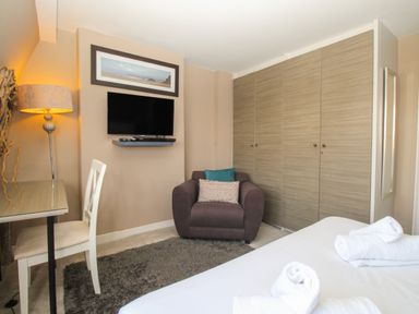 A bedroom with a bed and rolled towels a chair a desk a floor lamp a wall-mounted TV and a large wardrobe at Harbourside House in Brewers Quay Harbour