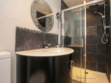 A bathroom with a curved vanity sink a round mirror a glass shower enclosure and black tile walls at Harbourside House Brewers Quay Harbour