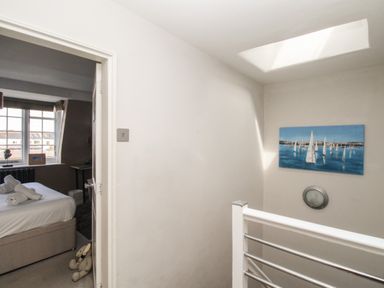 A stairwell with a skylight and painting of sailboats next to a bedroom with a bed and window at Harbourside House in Brewers Quay Harbour