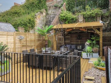 An outdoor patio with a dining table and chairs a covered seating area and potted plants at Harbourside House in Brewers Quay Harbour