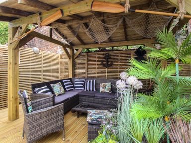 A covered outdoor seating area with wicker furniture cushions pillows and plants at Harbourside House in Brewers Quay Harbour