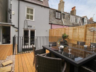An outdoor patio with a dining table and chairs surrounded by wooden decking and fencing at Harbourside House in Brewers Quay Harbour