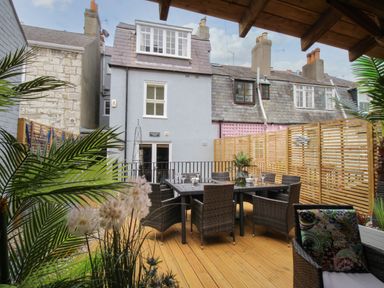 An outdoor patio with wicker chairs a table and plants surrounded by wooden fencing and buildings at Harbourside House in Brewers Quay Harbour