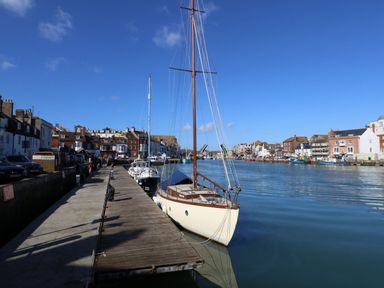 A dock with sailboats moored by a wooden pier along a waterfront with buildings on both sides at Harbourside House in Brewers Quay Harbour