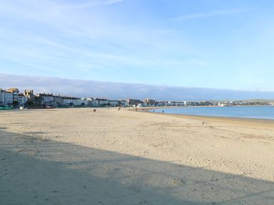 A sandy beach with a few people walking near the shoreline and buildings in the distance at Brewers Quay Harbour
