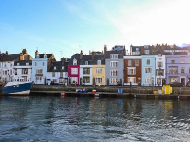 A row of multicolored buildings along a waterfront with a docked fishing boat at Brewers Quay Harbour