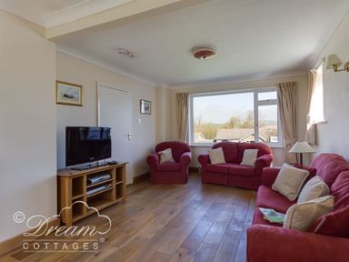 A living room with red sofas a wooden TV stand and a large window at Hillview Bungalow in Burton Bradstock