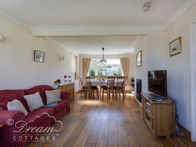 A living room with a red sofa cushions a dining table with wooden chairs and a television on a wooden stand at Hillview Bungalow in Burton Bradstock