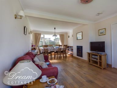 A living room with a red sofa a wooden dining table and chairs a television and a fireplace at Hillview Bungalow in Burton Bradstock
