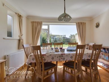 A dining room with a table and eight chairs by a window and sliding glass door at Hillview Bungalow Burton Bradstock