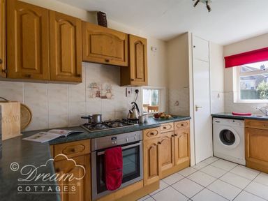 A kitchen with wooden cabinets a gas stove an oven a washing machine and a window with a red blind at Hillview Bungalow in Burton Bradstock