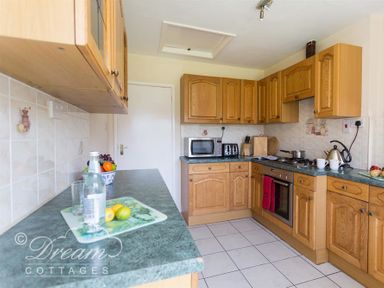 A kitchen with wooden cabinets microwave toaster oven and kettle at Hillview Bungalow in Burton Bradstock