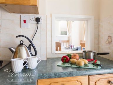 A kitchen counter with a kettle two cups vegetables a saucepan and a knife at Hillview Bungalow in Burton Bradstock