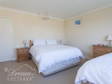 A bedroom with two beds bedside tables lamps and a framed picture on the wall at Hillview Bungalow in Burton Bradstock