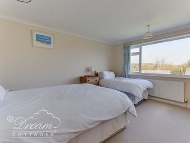 A bedroom with two single beds a wooden nightstand with a lamp and window with curtains at Hillview Bungalow in Burton Bradstock