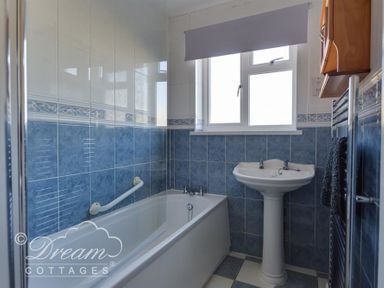 A bathroom with blue and white tiles a bathtub a pedestal sink a towel radiator and a window at Hillview Bungalow in Burton Bradstock