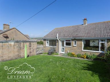 A backyard with grass lawn and flowers next to a single-story house at Hillview Bungalow in Burton Bradstock