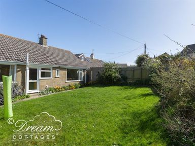 A backyard garden with a lawn and plants next to a single-story house at Hillview Bungalow in Burton Bradstock