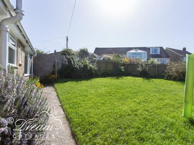 A backyard garden with a grass lawn and a paved path next to a house at Hillview Bungalow in Burton Bradstock