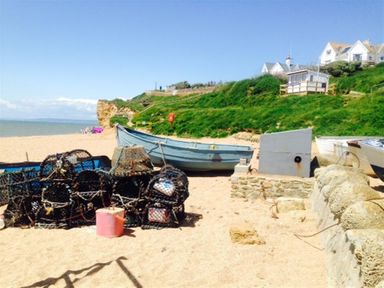 A beach with fishing nets and boats near grassy cliffs and houses at Hillview Bungalow in Burton Bradstock