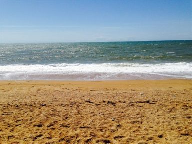 A sandy beach with waves and the sea under a clear blue sky at Hillview Bungalow in Burton Bradstock