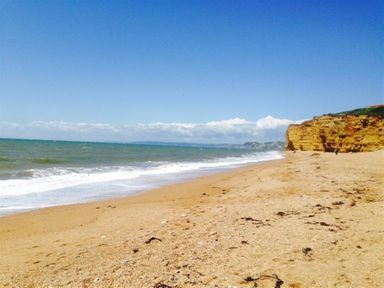 A sandy beach with cliffs on the side and the ocean under a blue sky at Hillview Bungalow in Burton Bradstock