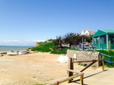 A beach with boats on the sand and a green tent with people sitting near it at Hillview Bungalow in Burton Bradstock