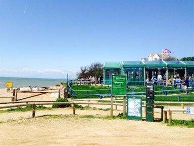 A beachside cafe with people sitting outside and a parking payment machine at Burton Bradstock
