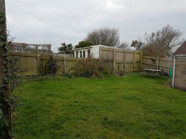 A backyard with grass a wooden fence a white shed and a wooden picnic table at Hillview Bungalow in Burton Bradstock
