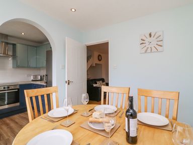 A dining table set with plates, glasses, bread, and a wine bottle in a kitchen with wooden chairs and light blue walls at Home Waters in Wyke Regis
