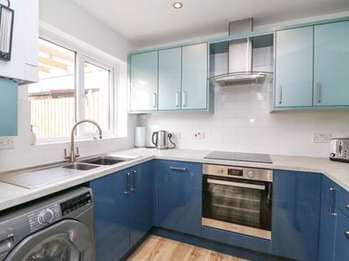 A kitchen with blue cabinets a washing machine a sink a kettle an oven and a toaster at Home Waters in Wyke Regis