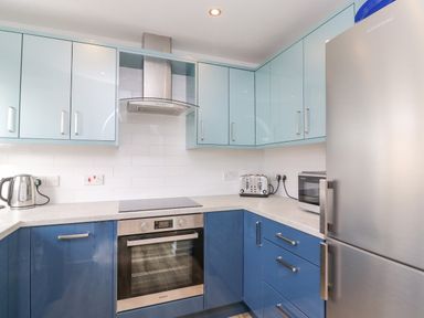 A kitchen with blue and light blue cabinets a stainless steel oven kettle toaster microwave and refrigerator at Home Waters in Wyke Regis