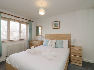A bedroom with a double bed with pillows and towels bedside tables lamps a window with blinds and curtains a dresser with a mirror and a framed picture on the wall at Home Waters in Wyke Regis