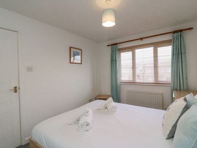 A bedroom with a bed folded towels on the bed wooden window blinds and blue curtains at Home Waters in Wyke Regis