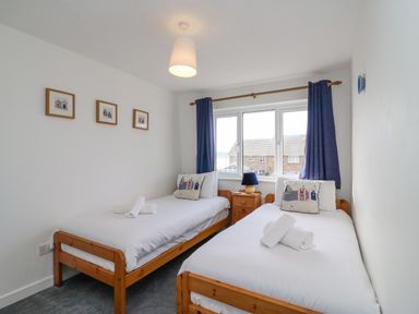 A bedroom with two single beds and a window with blue curtains at Home Waters in Wyke Regis