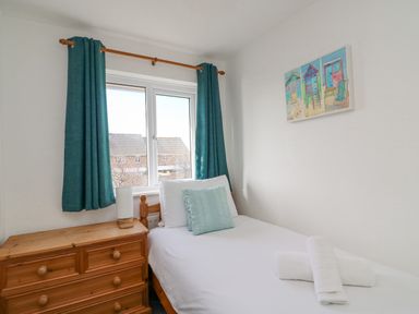 A small bedroom with a single bed next to a wooden chest of drawers and a window with teal curtains at Home Waters in Wyke Regis