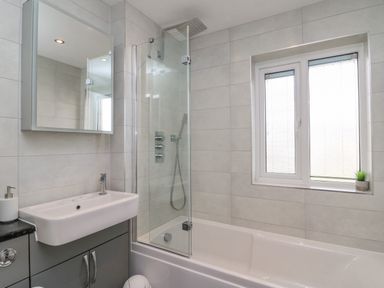 A bathroom with a bathtub shower combo a sink with cabinet and a window with blinds at Home Waters in Wyke Regis