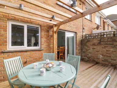 An outdoor patio with a round table and chairs under a wooden pergola at Home Waters in Wyke Regis
