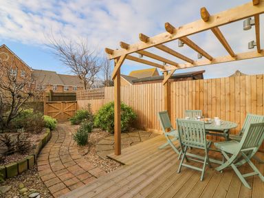 A backyard patio area with a wooden pergola and a table with four chairs at Home Waters in Wyke Regis