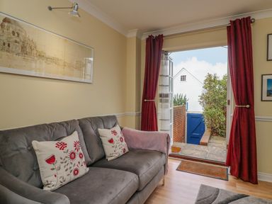A living room with a gray sofa and red floral cushions next to an open door with red curtains at Hops House in Brewers Quay Harbour