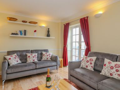 A living room with two gray sofas with floral pillows a wooden coffee table with a bottle and glasses and shelves on the wall at Hops House in Brewers Quay Harbour