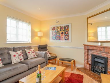 A living room with a gray sofa and patterned cushions a wooden coffee table with a bottle and glasses a fireplace and a colorful painting on the wall at Hops House in Brewers Quay Harbour