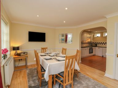 A dining room with a set table under a wall mounted TV next to a kitchen with white cabinets at Hops House Brewers Quay Harbour