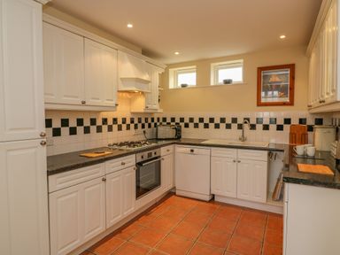 A kitchen with white cabinets black countertop tiled backsplash and terracotta floor at Hops House Brewers Quay Harbour